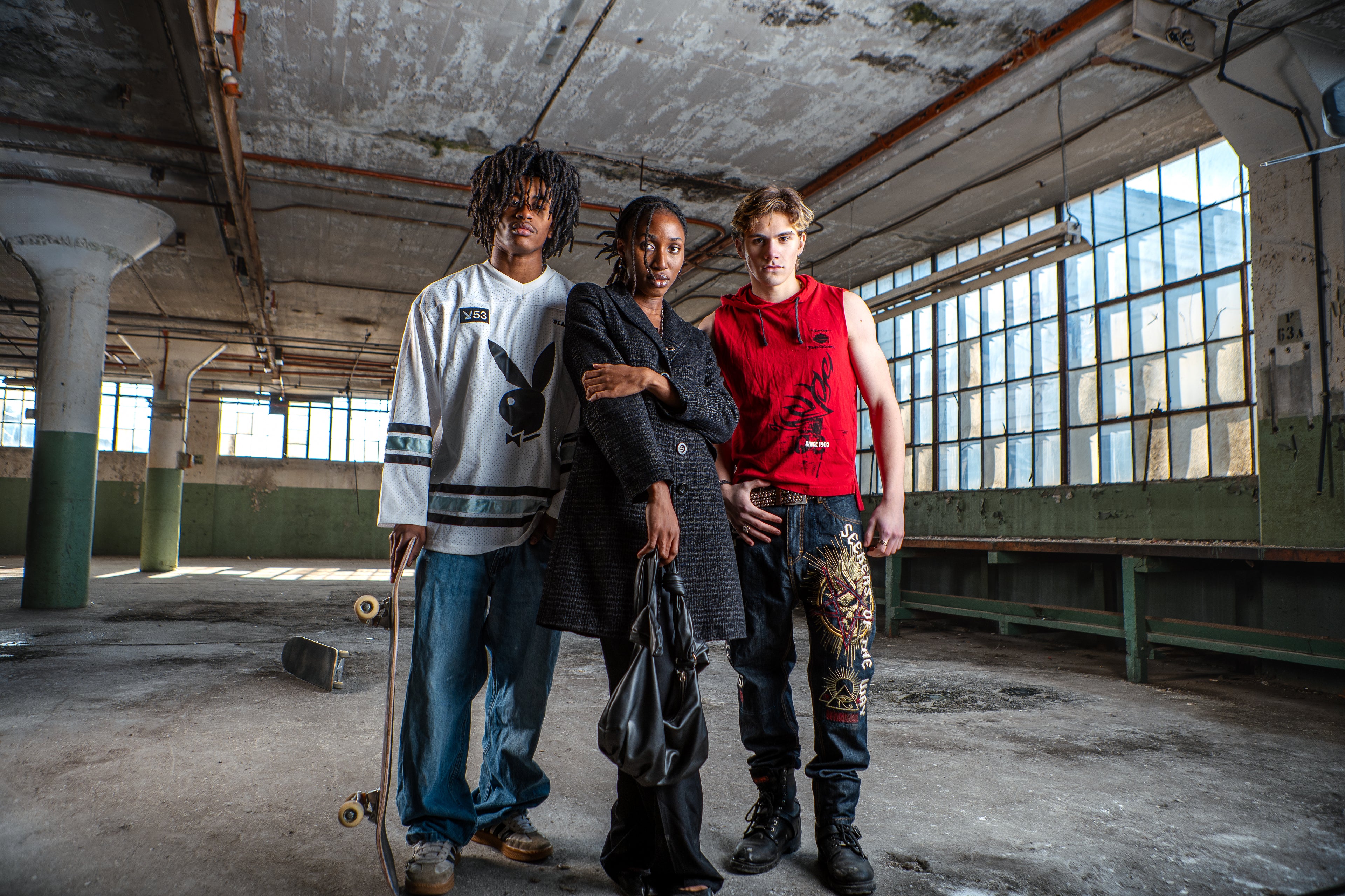 Three individuals standing in an industrial setting with large windows.